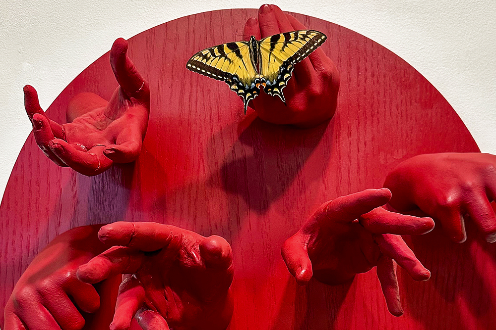 a portion of a sculpture depicting red hands coming out of a red circle with butterflies on some of the hands