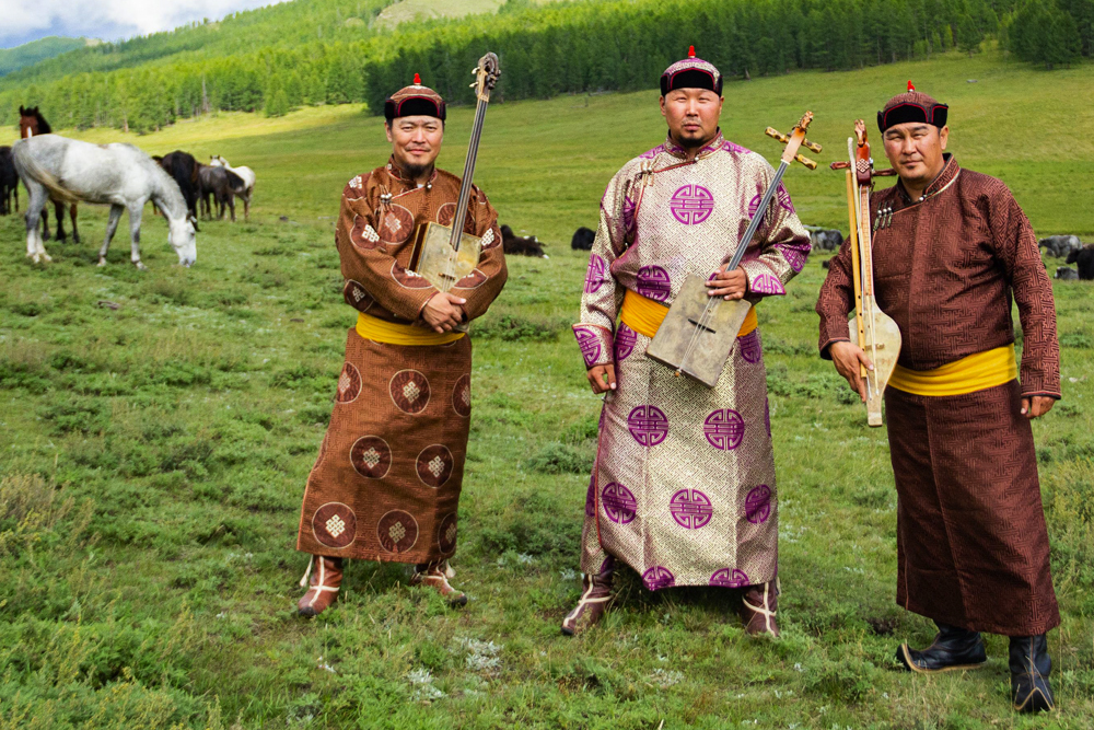 the three members of the group Alash standing in a field holding their musical instruments