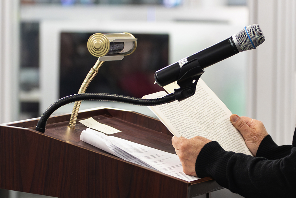 close up photo of an author's hands holding an open book at a podium with a microphone