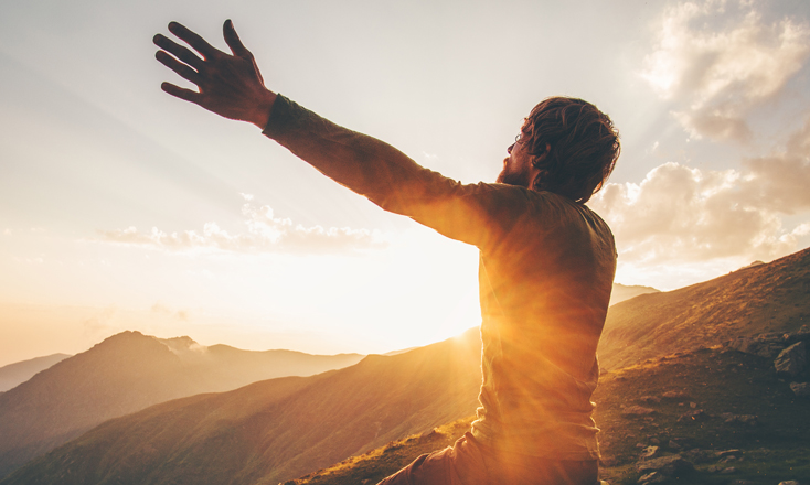a man sitting in the mountains at sunrise with his arms outstretched to the sky